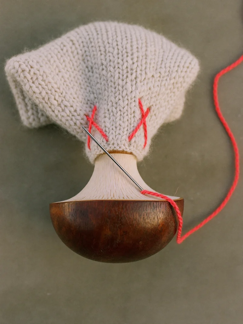 Strickpullover über einem Stopfpilz mit kontrastierendem Garn und Nadel
